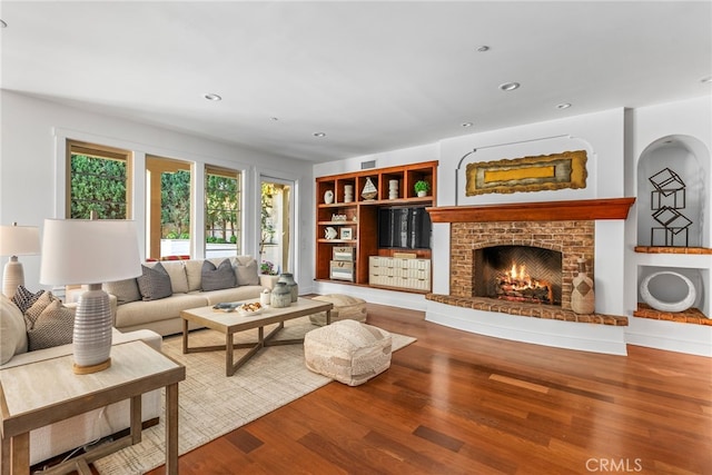 living room with hardwood / wood-style floors, built in features, and a brick fireplace