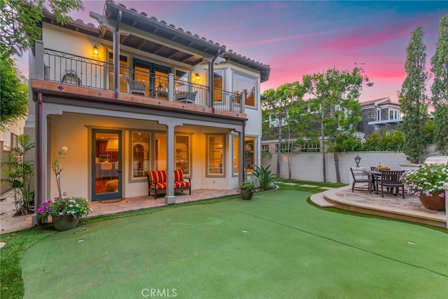 back house at dusk with a balcony and a patio