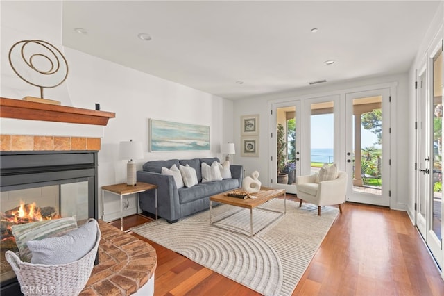 living room with a fireplace, french doors, a water view, and hardwood / wood-style flooring