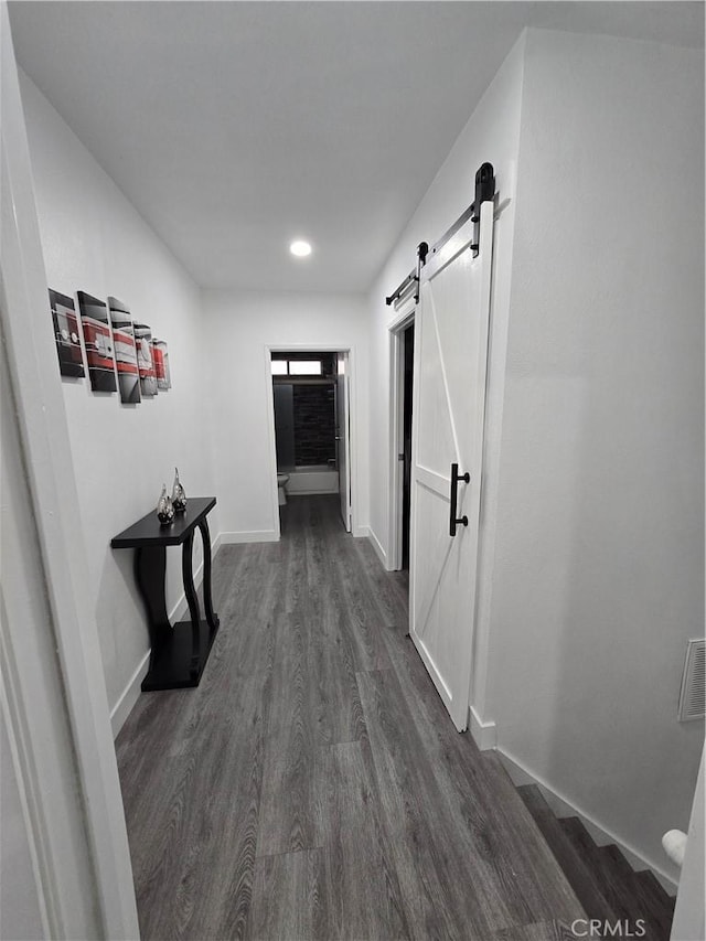 corridor with a barn door and dark hardwood / wood-style floors