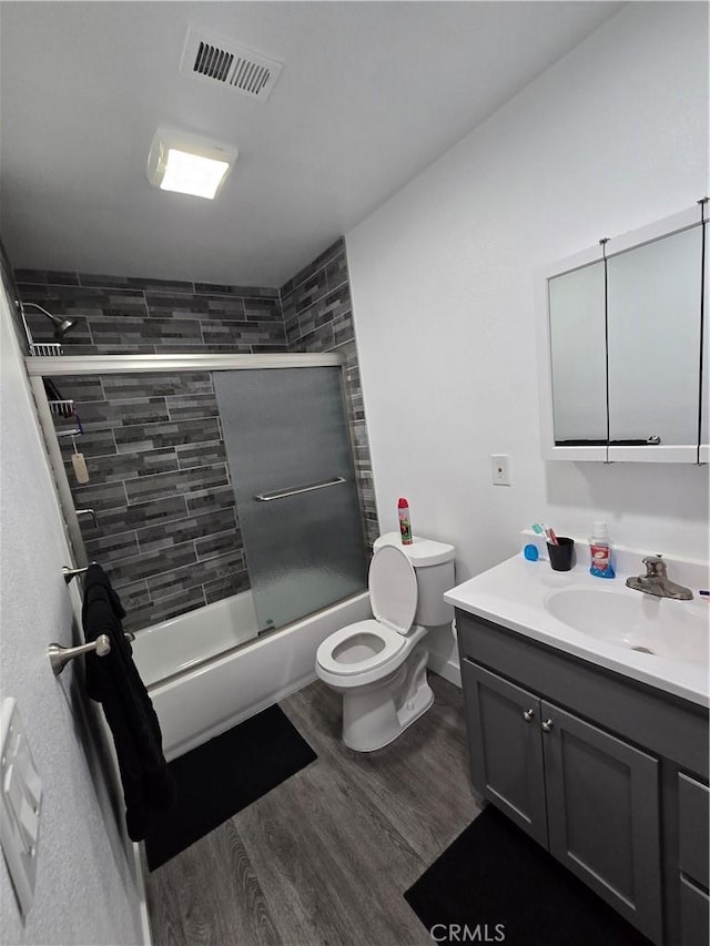 full bathroom with shower / bath combination with glass door, vanity, hardwood / wood-style flooring, and toilet