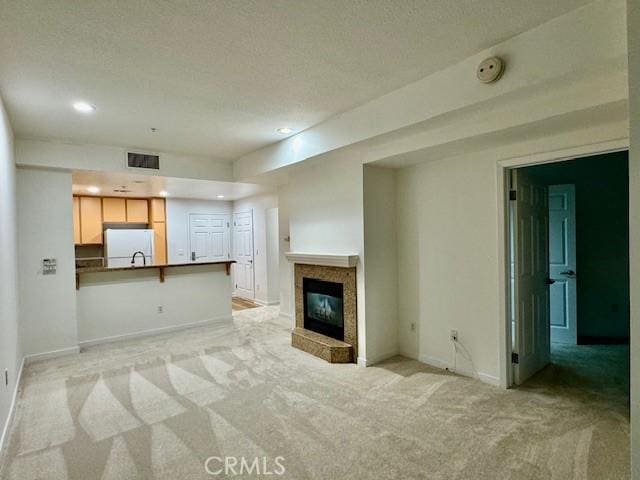 unfurnished living room with a textured ceiling, a fireplace, and light carpet