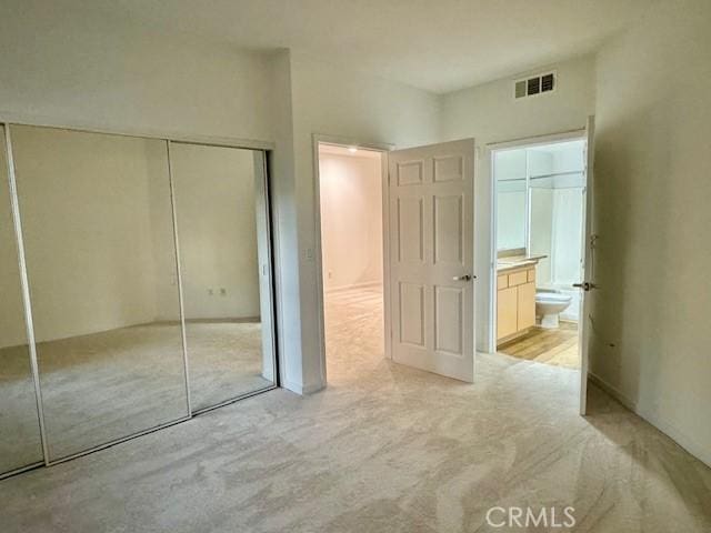 unfurnished bedroom featuring light carpet, ensuite bathroom, and a closet