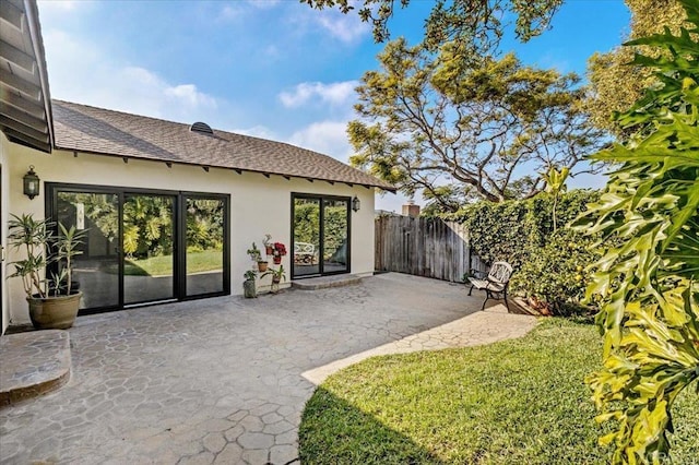 exterior space with fence, a yard, roof with shingles, stucco siding, and a patio area