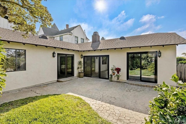 rear view of property featuring a shingled roof, a patio area, and stucco siding