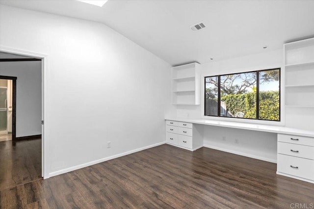 unfurnished office featuring vaulted ceiling, built in desk, dark wood-style flooring, and visible vents