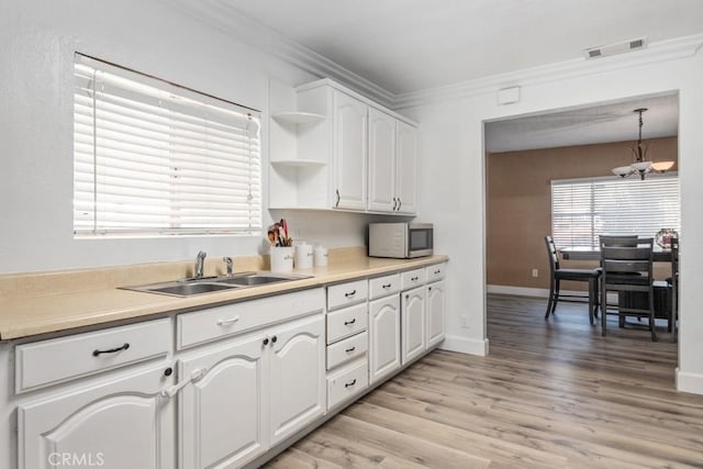 kitchen with pendant lighting, white cabinets, sink, light hardwood / wood-style flooring, and ornamental molding