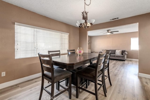 dining area featuring ceiling fan with notable chandelier, light wood-type flooring, and a textured ceiling