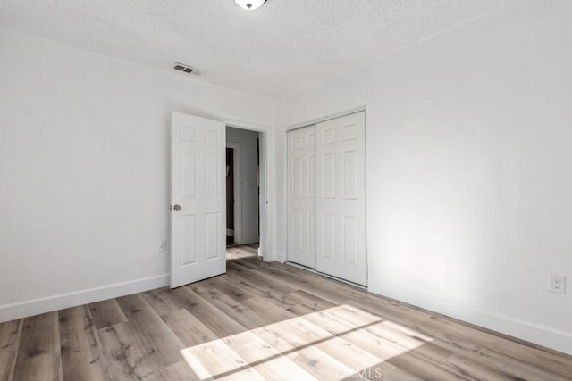 unfurnished bedroom with a textured ceiling, light wood-type flooring, and a closet