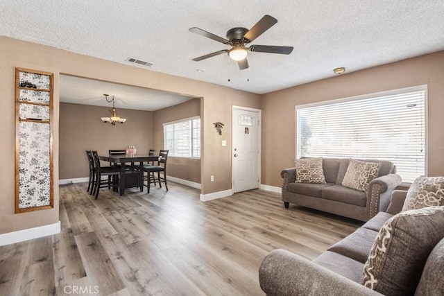 living room with ceiling fan with notable chandelier, light hardwood / wood-style floors, and a textured ceiling