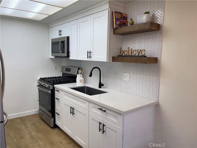 kitchen with a sink, open shelves, tasteful backsplash, appliances with stainless steel finishes, and light countertops