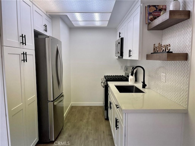 kitchen with open shelves, a sink, stainless steel appliances, light countertops, and light wood-type flooring