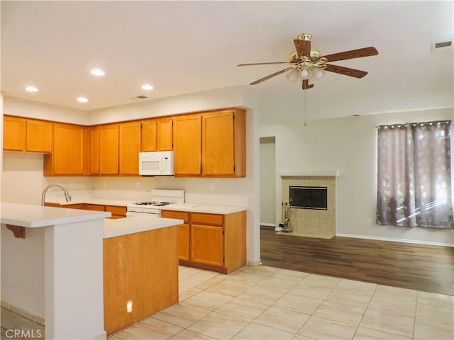 kitchen featuring ceiling fan, sink, kitchen peninsula, white appliances, and a fireplace