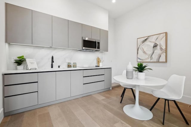 kitchen with sink, tasteful backsplash, light hardwood / wood-style floors, gray cabinets, and black electric stovetop