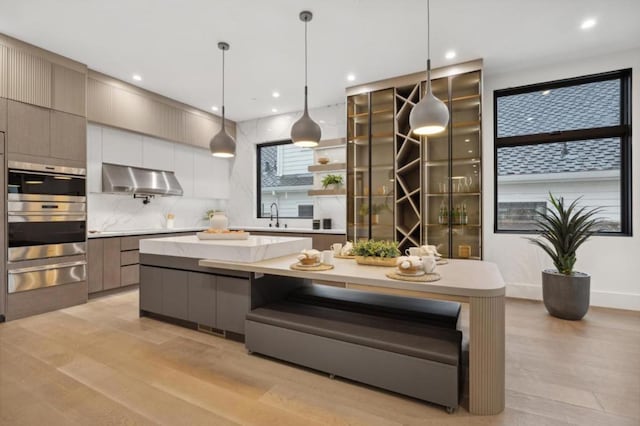 kitchen featuring a spacious island, light hardwood / wood-style flooring, pendant lighting, and ventilation hood