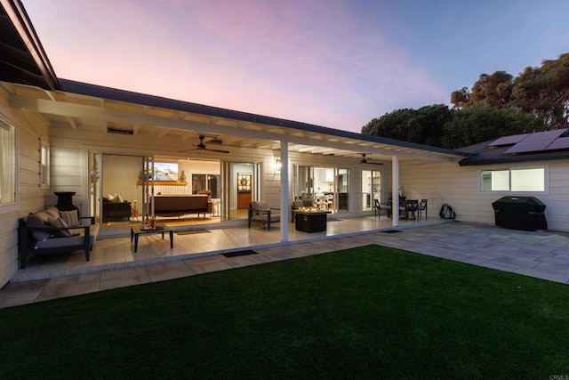 patio terrace at dusk featuring area for grilling, ceiling fan, and a yard