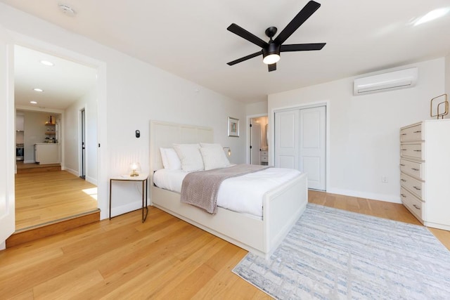 bedroom with a closet, light hardwood / wood-style floors, an AC wall unit, and ceiling fan