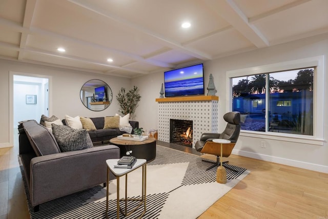 living room featuring beam ceiling, a tiled fireplace, wood-type flooring, and coffered ceiling