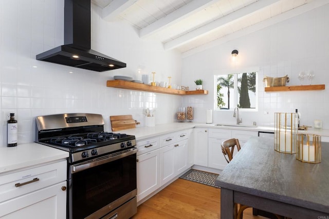 kitchen with tasteful backsplash, gas range, sink, wall chimney range hood, and white cabinetry