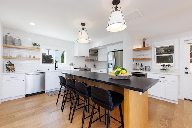 kitchen with stainless steel appliances, a kitchen island, pendant lighting, light hardwood / wood-style flooring, and white cabinetry