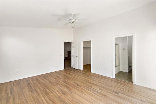 unfurnished bedroom with light wood-type flooring, ensuite bath, a spacious closet, and ceiling fan