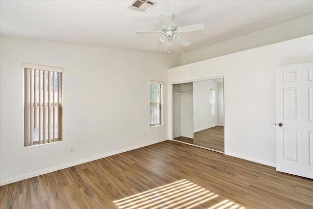 unfurnished bedroom featuring wood-type flooring, a closet, multiple windows, and ceiling fan