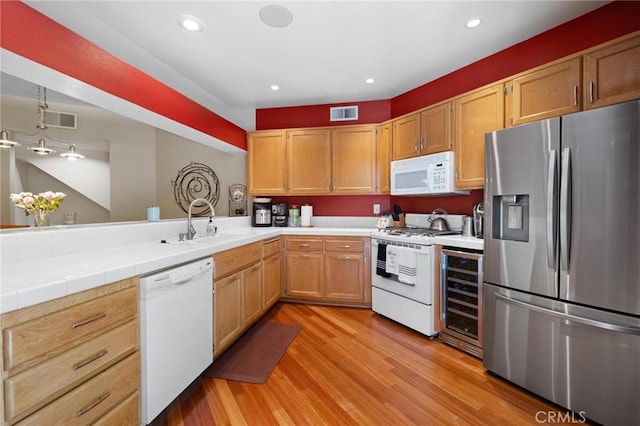 kitchen featuring sink, beverage cooler, light hardwood / wood-style floors, decorative light fixtures, and white appliances