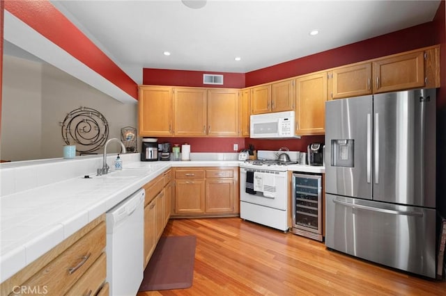 kitchen with tile counters, sink, beverage cooler, light hardwood / wood-style floors, and white appliances