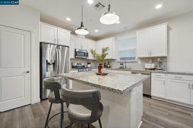 kitchen featuring appliances with stainless steel finishes, hardwood / wood-style flooring, white cabinetry, and pendant lighting