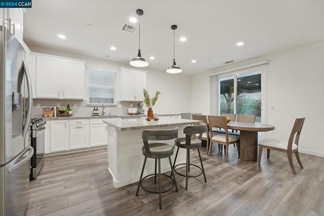 kitchen with decorative light fixtures, stainless steel appliances, a kitchen island, and white cabinetry