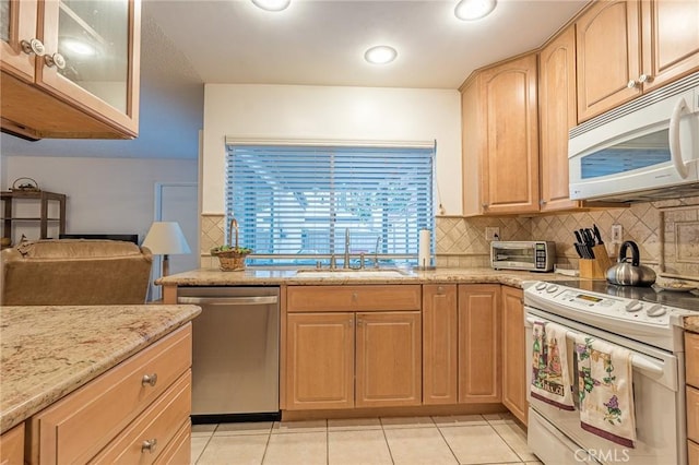 kitchen with sink, white appliances, backsplash, light stone countertops, and light brown cabinetry