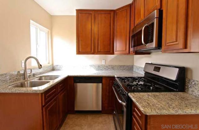 kitchen with light stone countertops, kitchen peninsula, stainless steel appliances, sink, and light tile patterned flooring