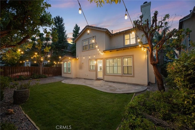 back house at dusk with a lawn and a patio