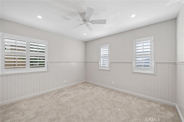 empty room with light colored carpet, ceiling fan, and wood walls