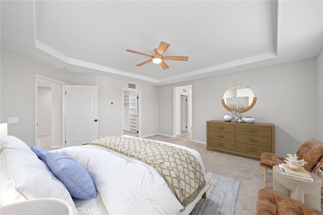 carpeted bedroom featuring a tray ceiling, a spacious closet, a closet, and ceiling fan