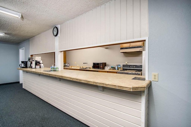 kitchen with range, a textured ceiling, tile countertops, and dark carpet