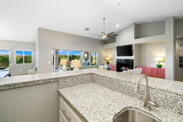 kitchen featuring lofted ceiling, sink, ceiling fan, light stone countertops, and a tiled fireplace