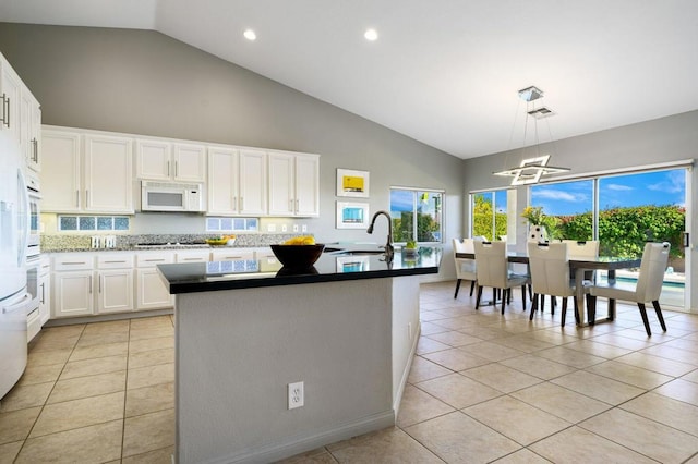 kitchen with white cabinets, light tile patterned flooring, white appliances, and an island with sink