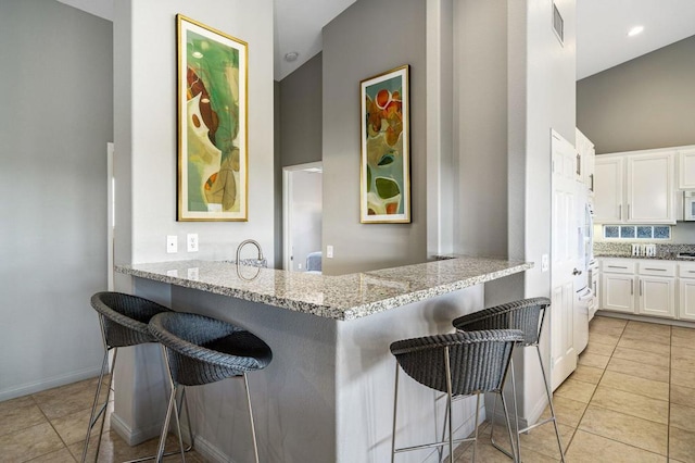 kitchen with light stone countertops, a kitchen bar, kitchen peninsula, and white cabinets