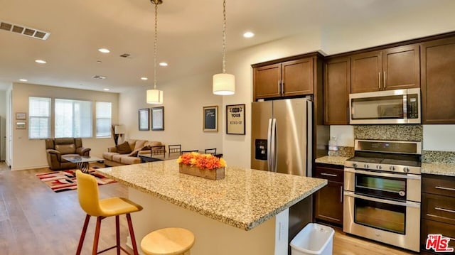 kitchen featuring appliances with stainless steel finishes, dark brown cabinetry, light hardwood / wood-style floors, and light stone counters