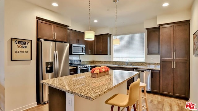 kitchen featuring hanging light fixtures, light stone countertops, light hardwood / wood-style floors, appliances with stainless steel finishes, and a kitchen island