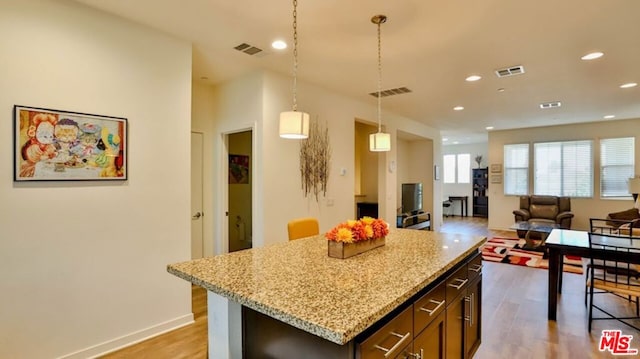 kitchen with a center island, hanging light fixtures, light hardwood / wood-style floors, light stone counters, and dark brown cabinetry