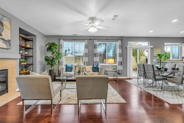 living room featuring a tiled fireplace, a wealth of natural light, built in features, and ceiling fan