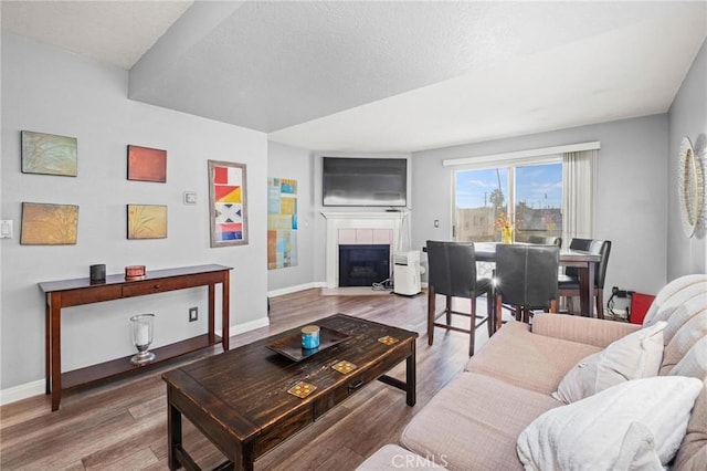 living room featuring hardwood / wood-style floors, a textured ceiling, and a tiled fireplace