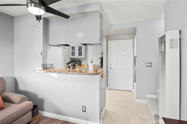 kitchen with white cabinetry, light stone counters, white refrigerator, kitchen peninsula, and light wood-type flooring