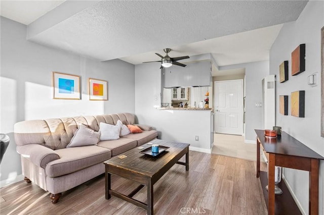 living room featuring ceiling fan, a textured ceiling, and light wood-type flooring