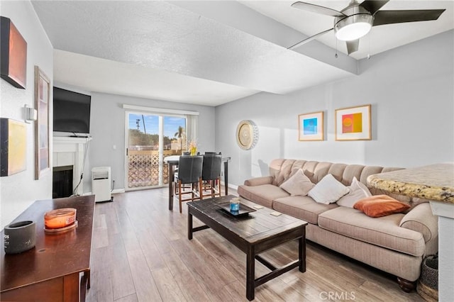 living room with ceiling fan, a textured ceiling, and light hardwood / wood-style flooring