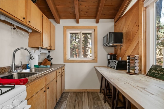 kitchen featuring beam ceiling, stove, a sink, wooden ceiling, and baseboards