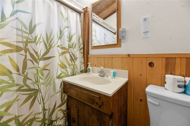 full bathroom featuring a wainscoted wall, a textured wall, toilet, wood walls, and vanity