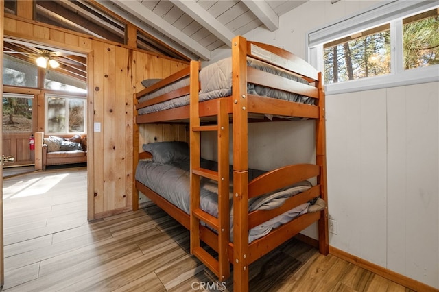 bedroom with wooden walls, lofted ceiling with beams, and wood finished floors